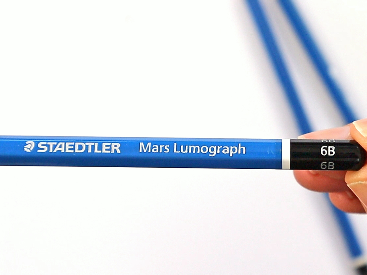 Photo showing a hand holding a blue Staedtler Mars Lumograph graphite pencil